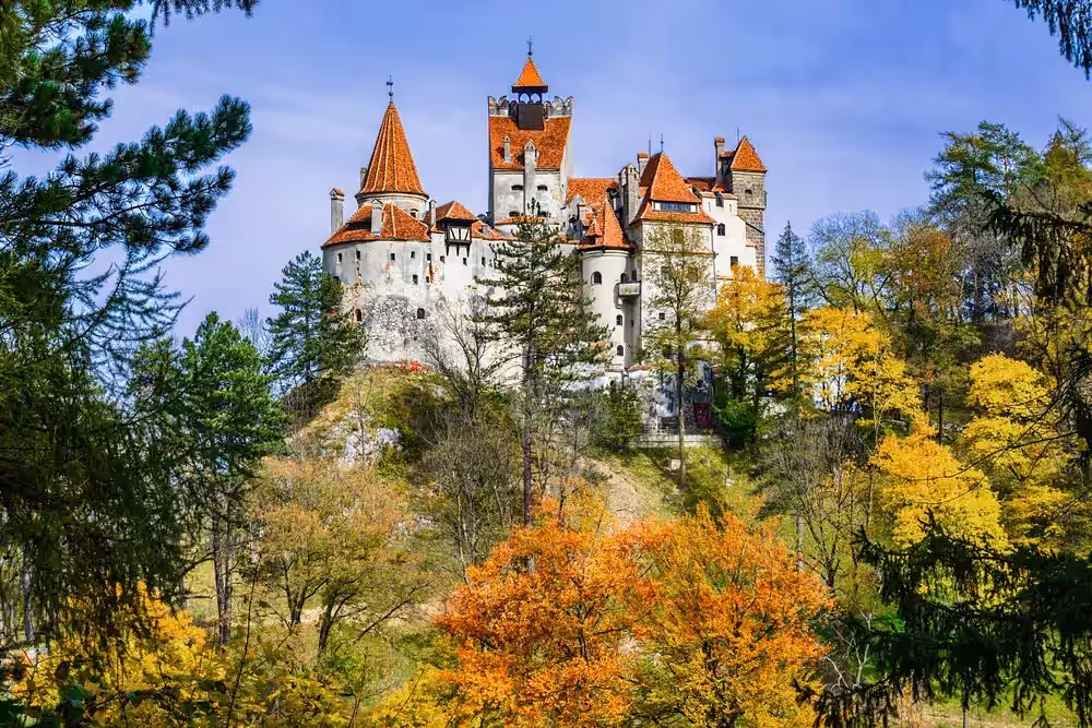Castelul Bran toamna, cu turnuri roșii deasupra copacilor galbeni Castelul Bran toamna, cu turnuri roșii deasupra copacilor galbeni