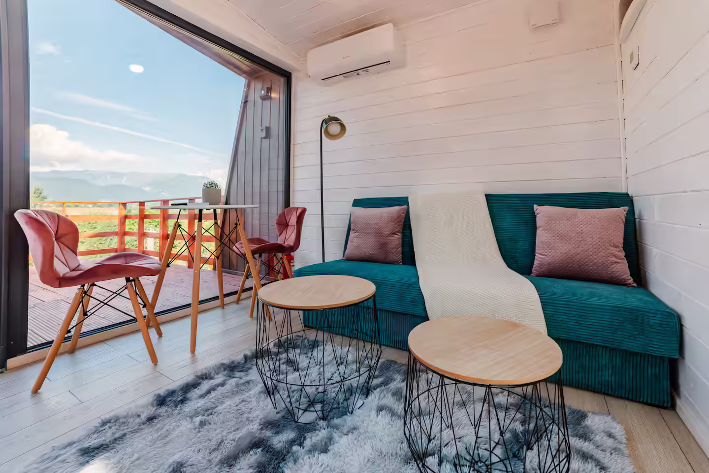 Interiorul cabanei SkyAtlas Hideaway cu canapea turcoaz, masă de cafea și ferestre mari Interiorul cabanei SkyAtlas Hideaway cu canapea turcoaz, masă de cafea și ferestre mari