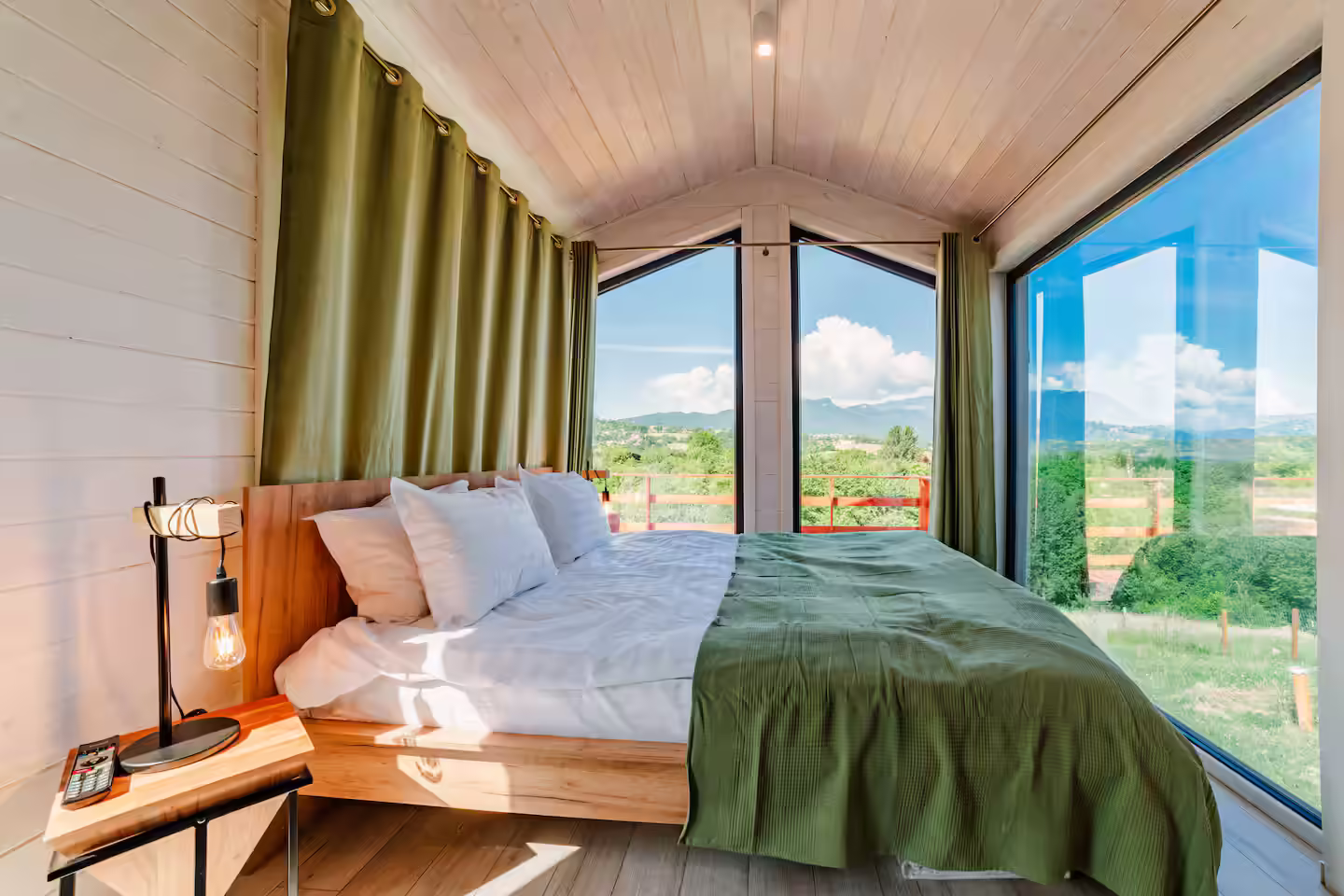 Dormitor cu pat dublu, perdele verzi și lampă de citit în cabana SkyAtlas Hideaway Dormitor cu pat dublu, perdele verzi și lampă de citit în cabana SkyAtlas Hideaway