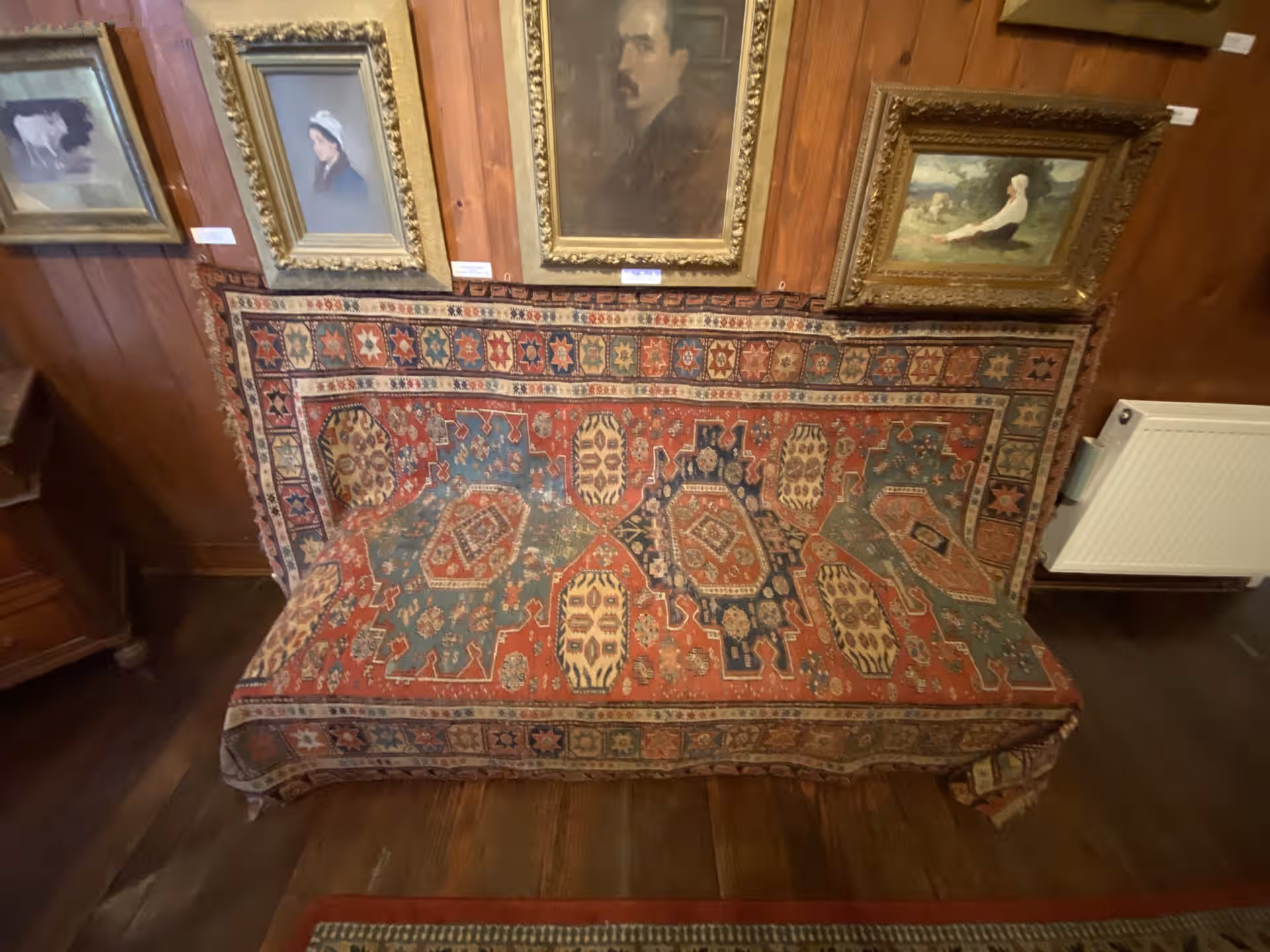 Covor oriental și tablouri de Grigorescu pe pereții din lemn ai casei