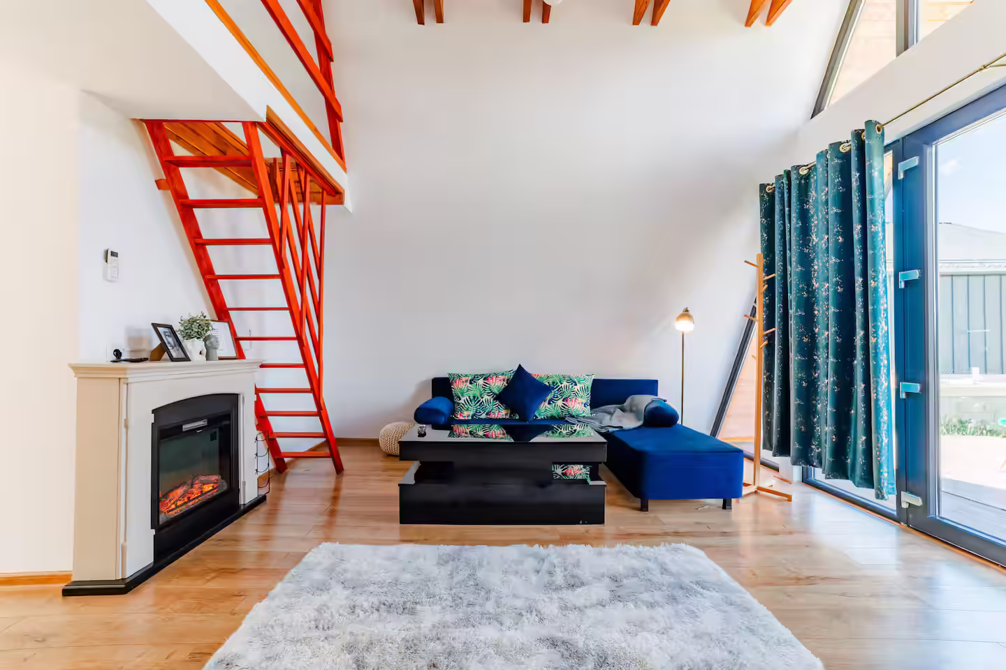 Living luminos în cabana A-frame SkyAtlas Hideaway, cu șemineu și scară roșie spre mansardă Living luminos în cabana A-frame SkyAtlas Hideaway, cu șemineu și scară roșie spre mansardă