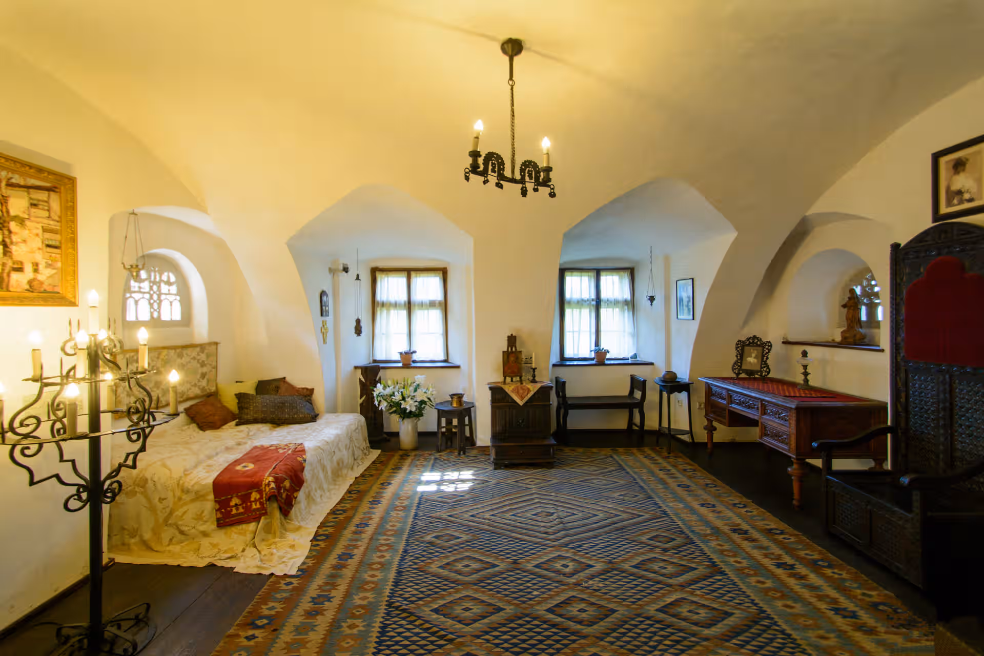 Dormitor luminos cu covor tradițional și candelabru în Castelul Bran Dormitor luminos cu covor tradițional și candelabru în Castelul Bran