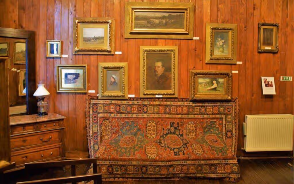 Perete cu tablouri și covor tradițional în casa lui Nicolae Grigorescu