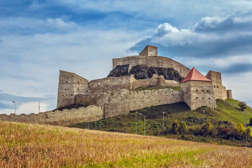Cetatea Rupea pe deal sub cer albastru cu nori