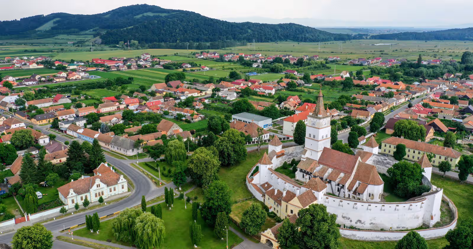 Satul Hărman și cetatea țărănească văzute din dronă, cu dealurile Brașovului