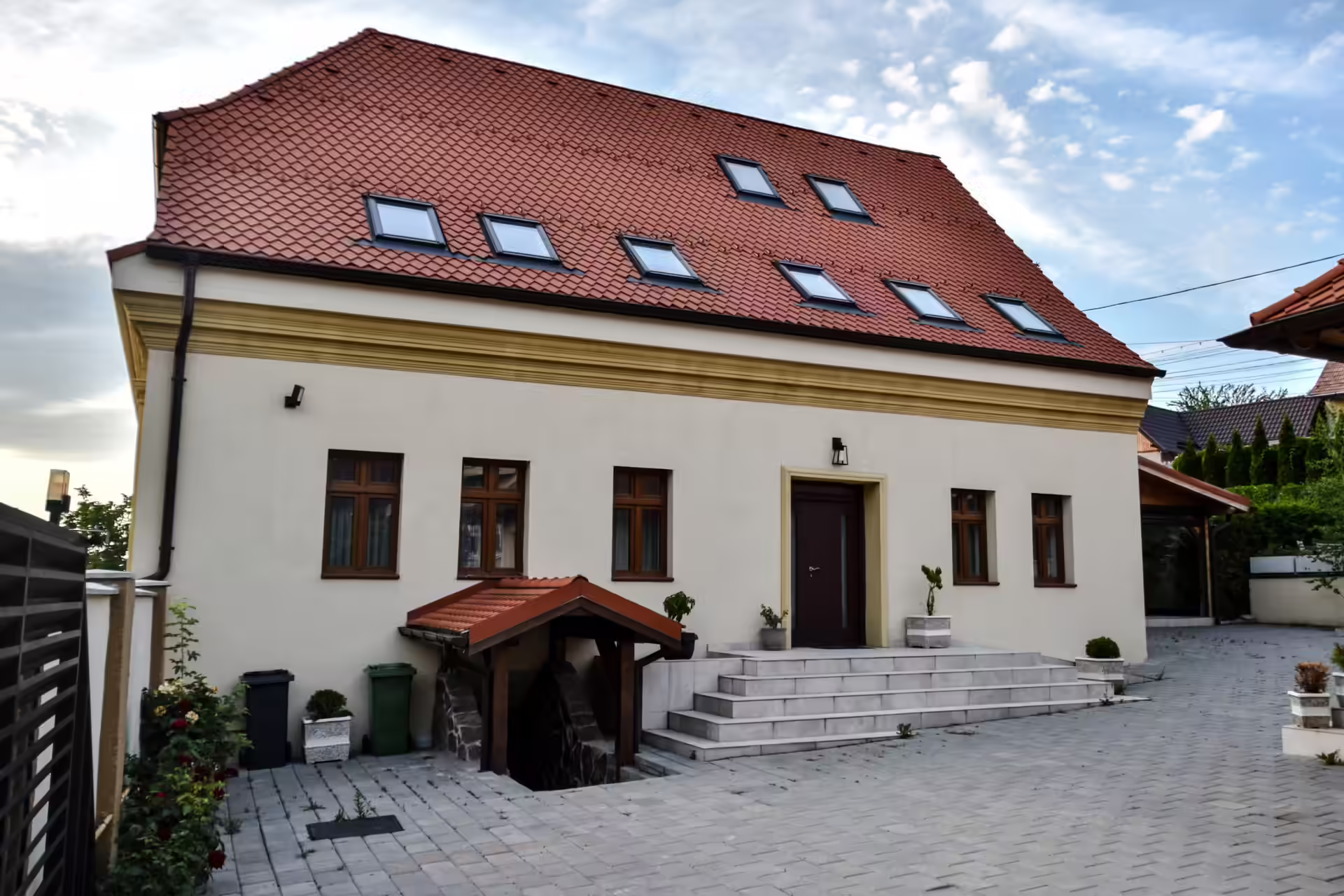 Fațada principală a vilei Berg House 31 din Săcele, cu acoperiș roșu și curte pavată Fațada principală a vilei Berg House 31 din Săcele, cu acoperiș roșu și curte pavată