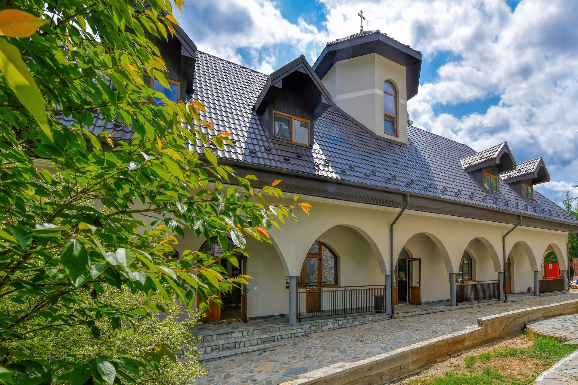 Arcadele chiliilor Mănăstirii Caraiman printre crengi verzi Arcadele chiliilor Mănăstirii Caraiman printre crengi verzi